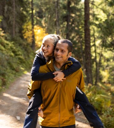 Vater trägt sein Kind huckepack auf einem sonnigen Waldweg
