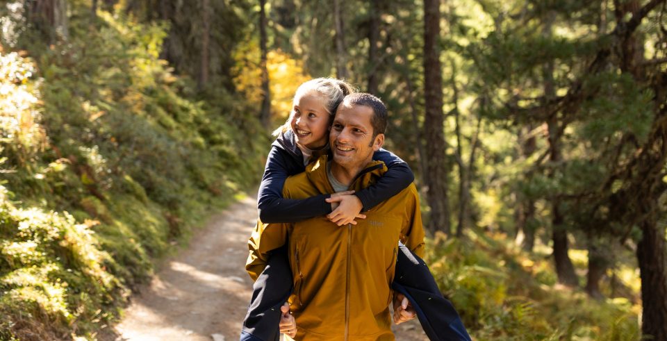 Vater trägt sein Kind huckepack auf einem sonnigen Waldweg