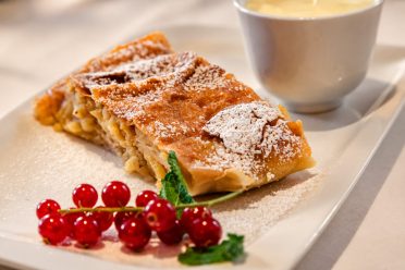 Apple strudel with icing sugar, redcurrants and a cup of vanilla sauce at Hotel DreiSonnen in Serfaus.