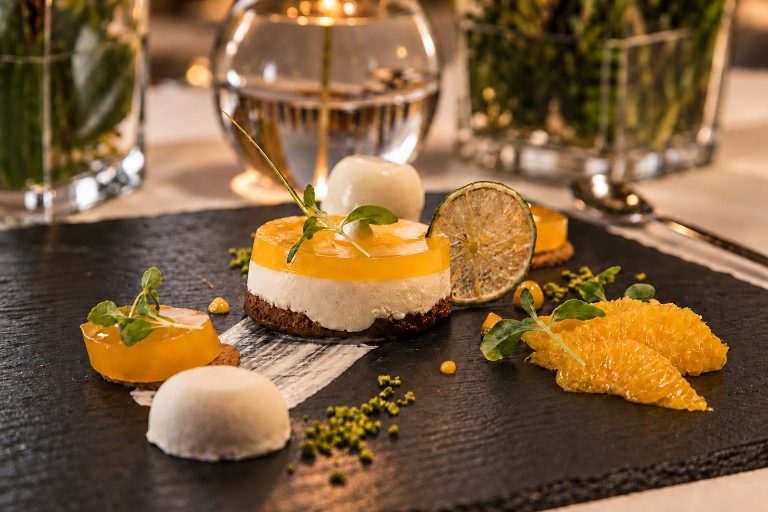 Quark dessert with poppy seeds, orange segments and sorbet on a slate board.