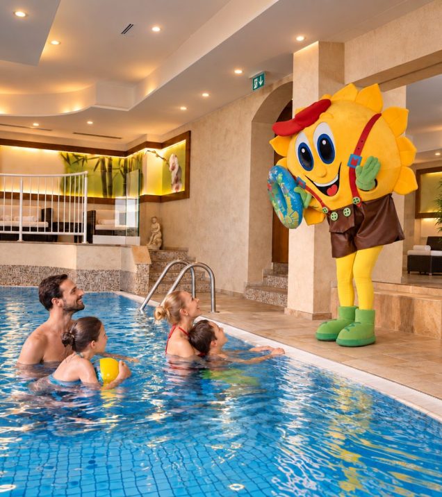Familie im Hallenbad blickt zum Maskottchen Sonni am Beckenrand.