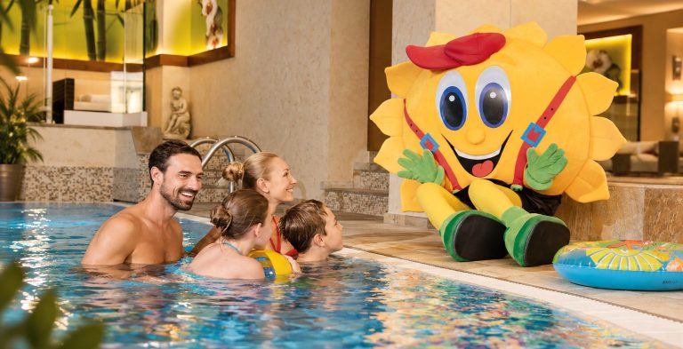 Family with two children and mascot Sonni in the indoor pool of Hotel DreiSonnen in Serfaus