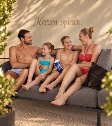 Familie mit zwei Kindern sitzt gemeinsam auf einem Sofa im Ruhebereich.