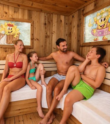 Eine Familie sitzt gemeinsam in der Familiensauna mit Sonni-Wandbildern im Hotel DreiSonnen in Serfaus.
