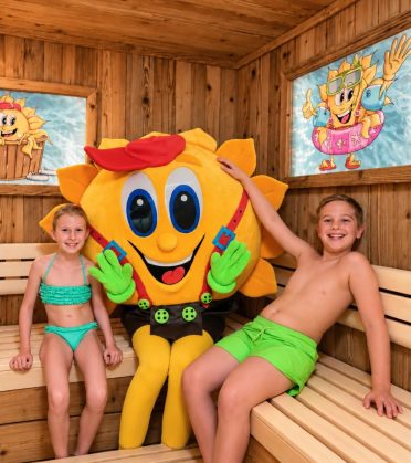 Maskottchen Sonni mit zwei Kindern auf der Bank der Familiensauna im Hotel DreiSonnen in Serfaus