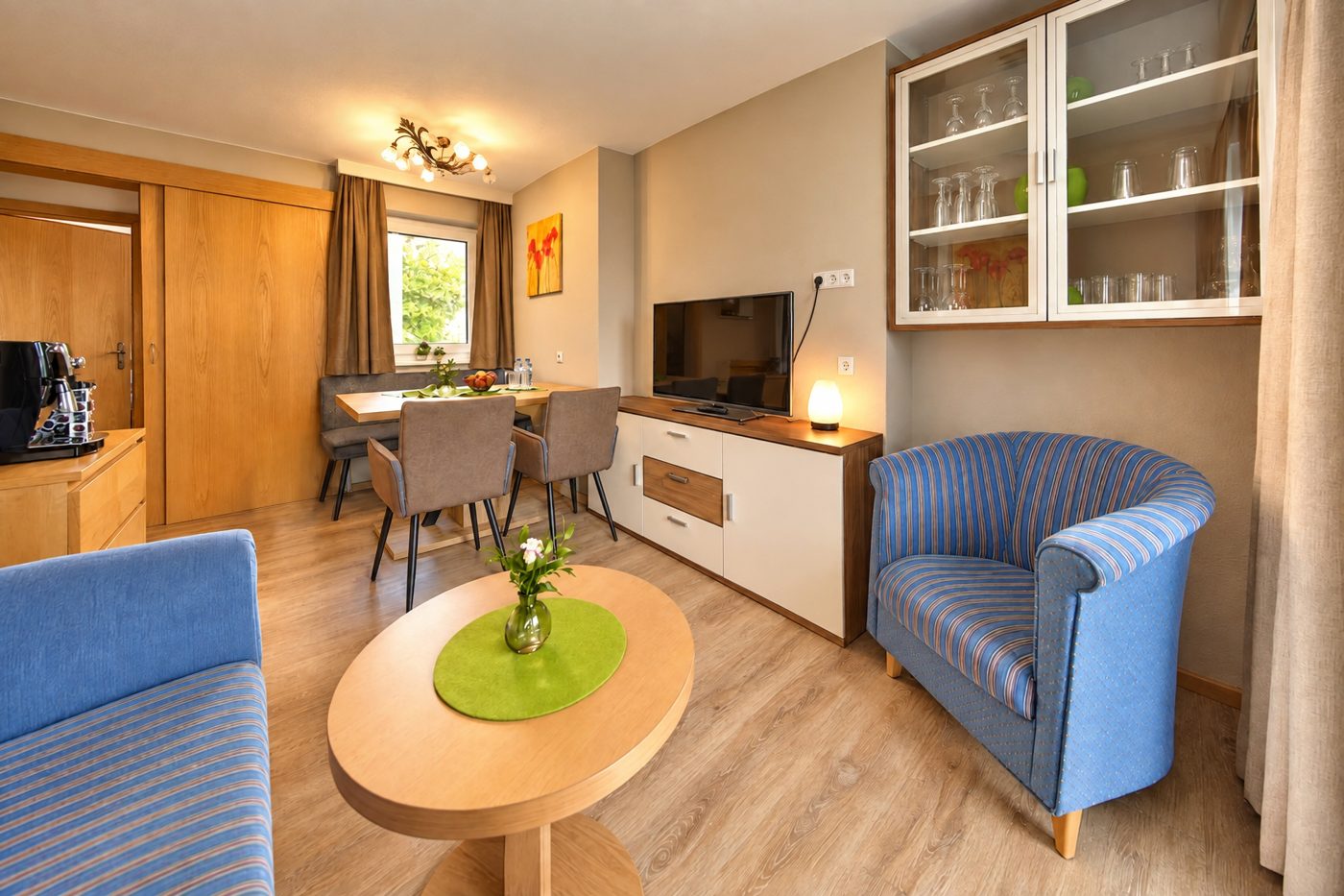 Living area with blue armchair, oval coffee table, display cabinet and TV in Apartment Anneliese at Hotel DreiSonnen in Serfaus