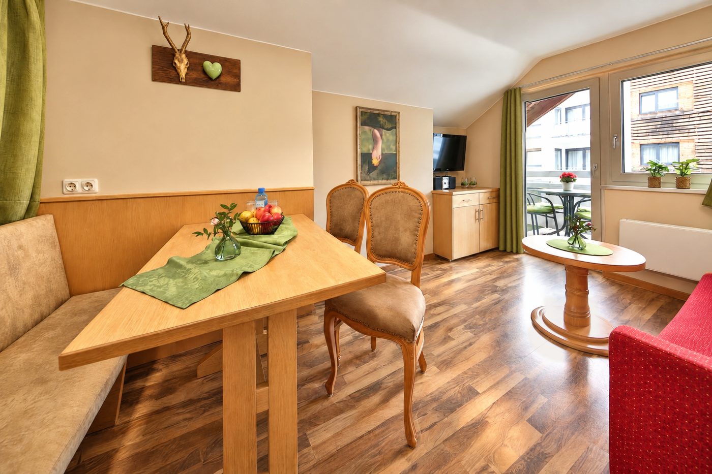 Essbereich mit Eckbank und Holztisch, Wohnbereich und Balkontür unter der Dachschräge in der Ferienwohnung Irene des Hotels DreiSonnen in Serfaus