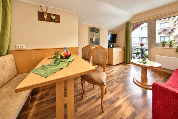Dining area with corner bench and wooden table, living area and balcony door under the sloping roof in Apartment Irene at Hotel DreiSonnen in Serfaus