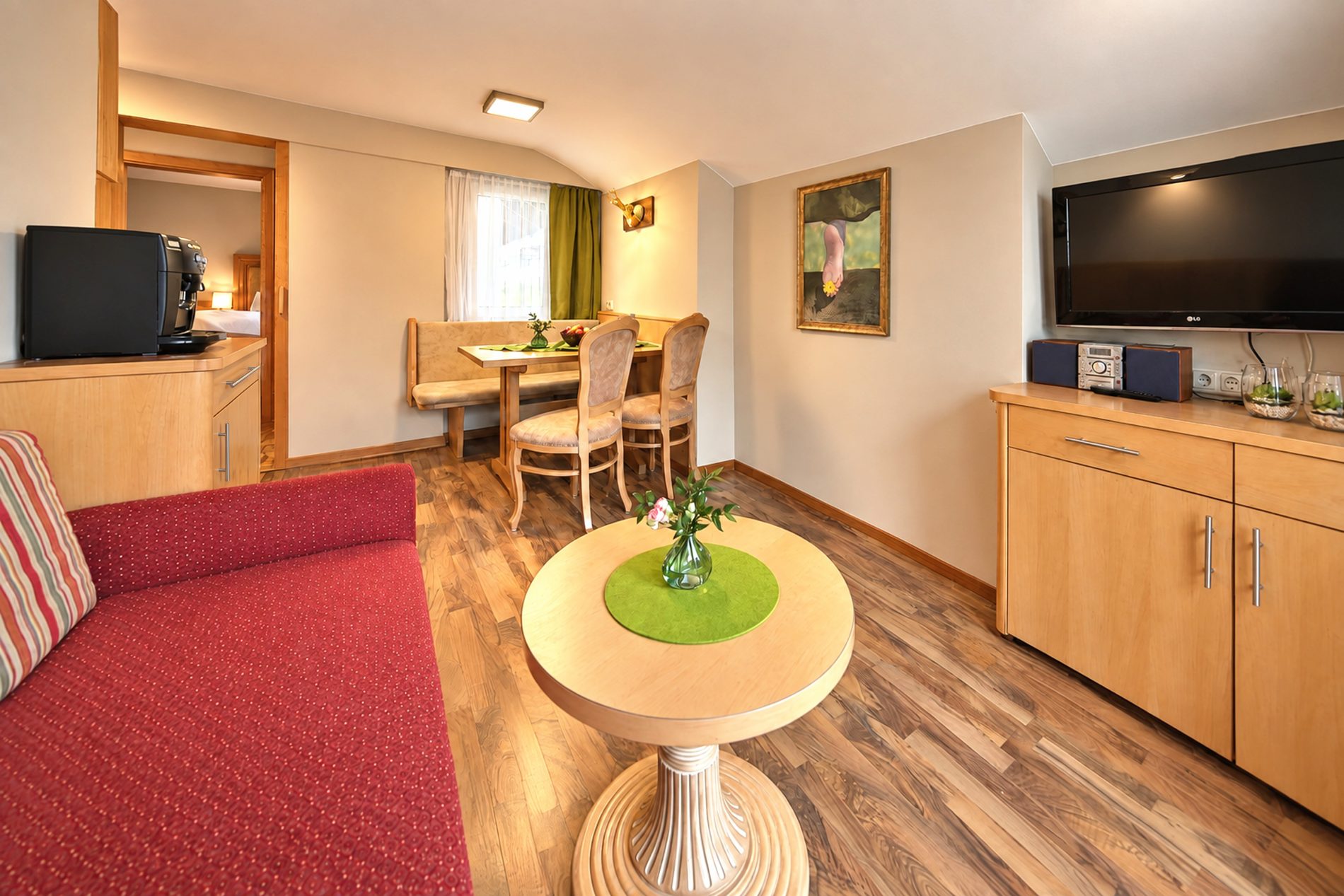 Wohnbereich mit rotem Sofa, rundem Beistelltisch, TV und Blick zum Essbereich in der Ferienwohnung Irene des Hotels DreiSonnen in Serfaus
