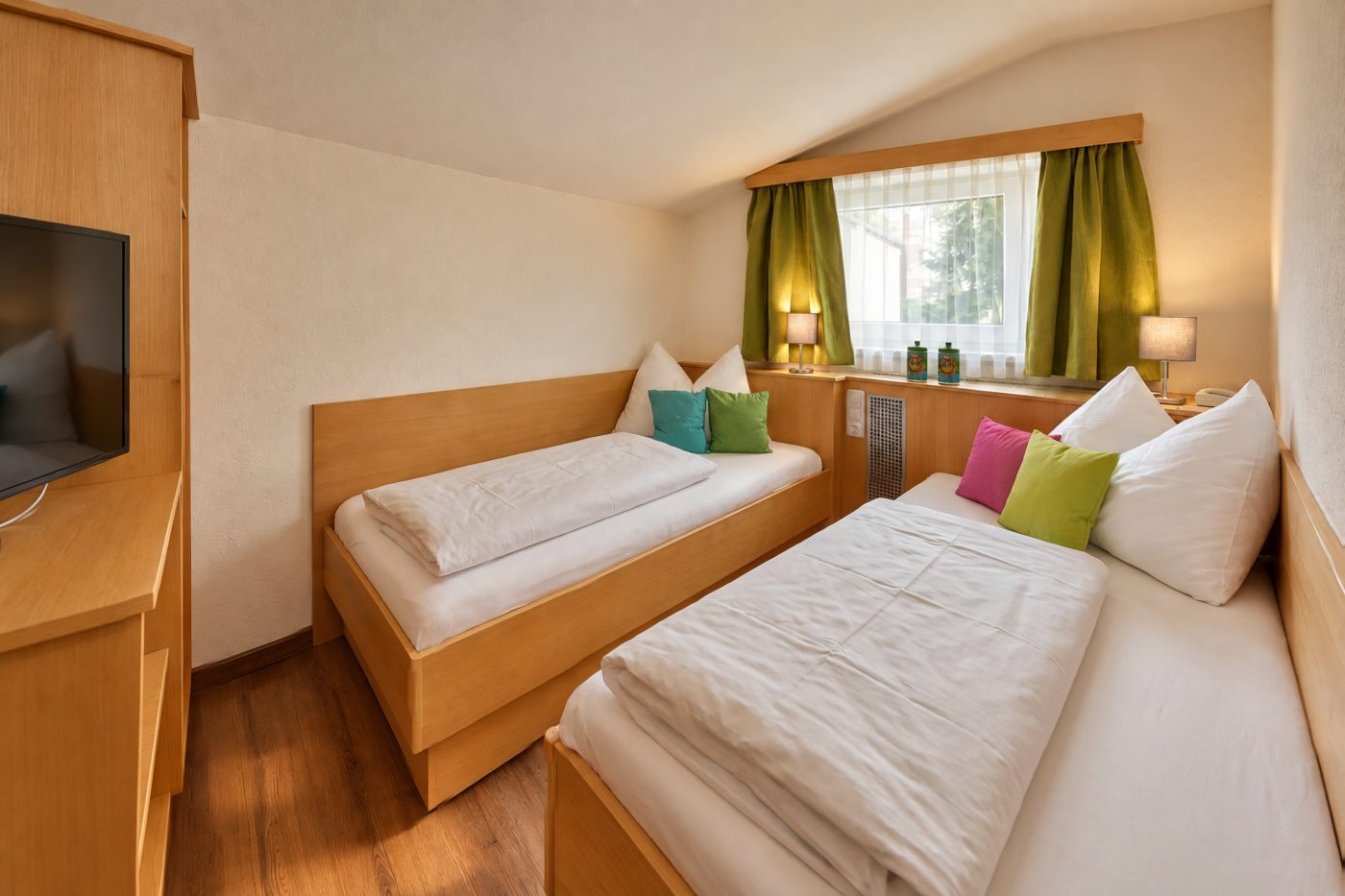 Zwei Einzelbetten unter dem Fenster mit grünen Vorhängen in der Ferienwohnung Irene des Hotels DreiSonnen in Serfaus