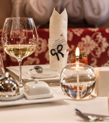 Gedeckter Tisch mit Weißweinglas, Kerze und gefalteter Serviette.