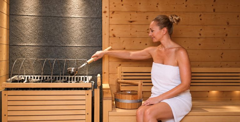 Woman pouring water from the ladle onto the stones in the sauna of Hotel DreiSonnen.