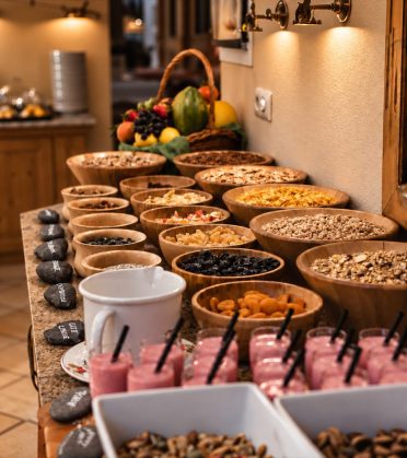 Muesli bar with wooden bowls full of flakes, nuts and dried fruit at the breakfast buffet at Hotel DreiSonnen.