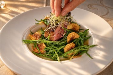 A hand arranging cress on a plate with meat, beans and croutons, at Hotel DreiSonnen in Serfaus.