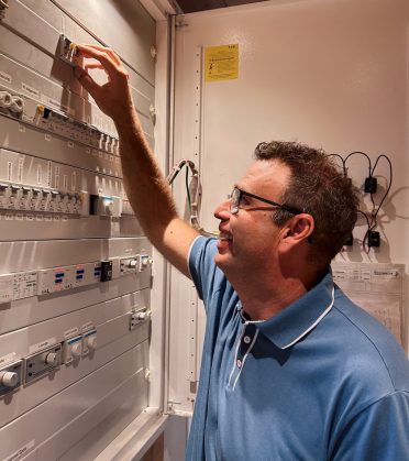 A man in a blue polo shirt working at the control cabinet of the building services at Hotel DreiSonnen.