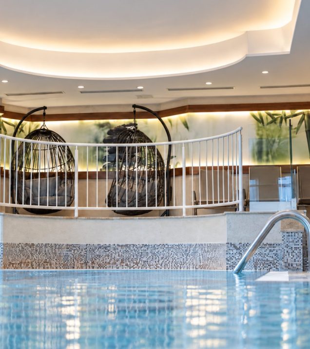 Indoor pool with hanging chairs and a mosaic wall in the DreiSonnen Wellnesswelt.