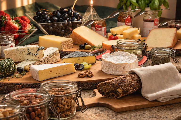 Cheese buffet with grapes, nuts and fruit on wooden boards.