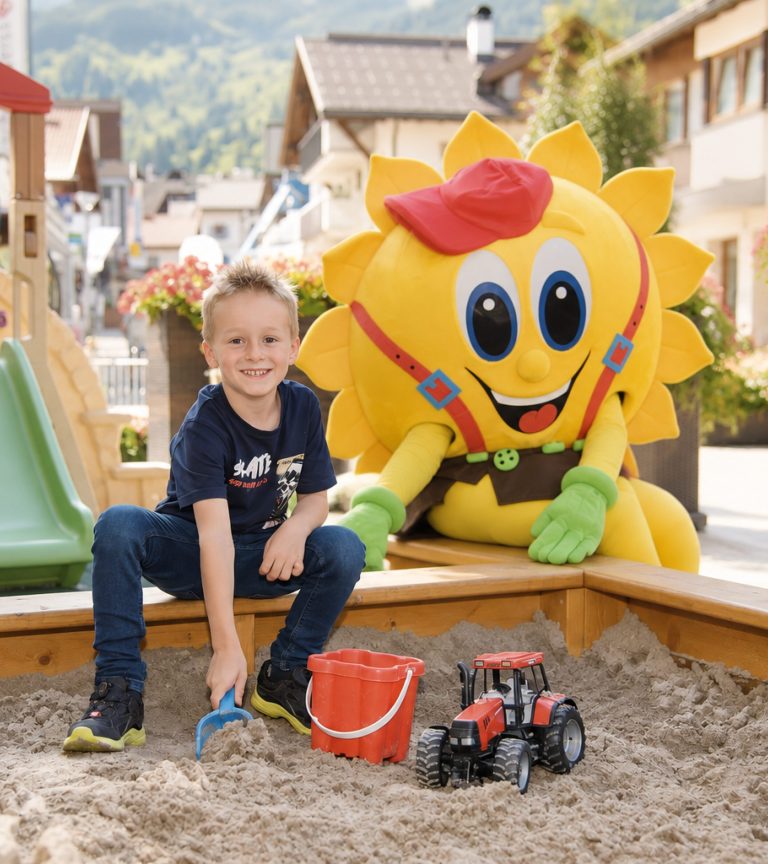 A child playing with the mascot Sonni in the sandpit at the playground of Hotel DreiSonnen in Serfaus