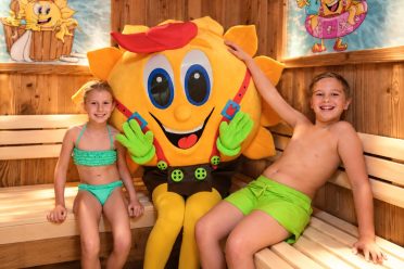 Zwei Kinder sitzen mit dem Maskottchen Sonni in der Familiensauna