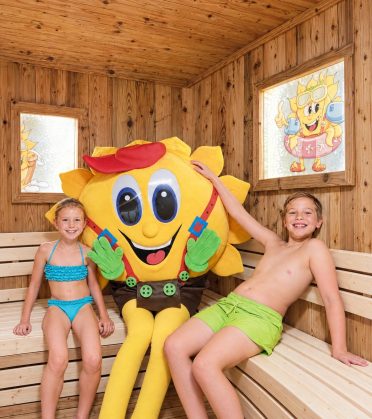 Zwei Kinder sitzen mit dem Maskottchen Sonni in der Familiensauna.