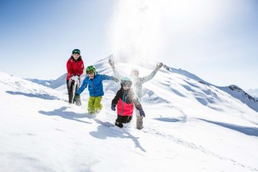 Kinder werfen auf dem verschneiten Rücken den Schnee in die Luft.