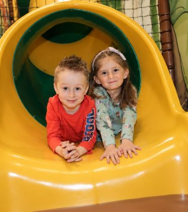 Zwei Kinder in der gelben Tunnelrutsche der Spiel- und Erlebniswelt im Hotel DreiSonnen in Serfaus