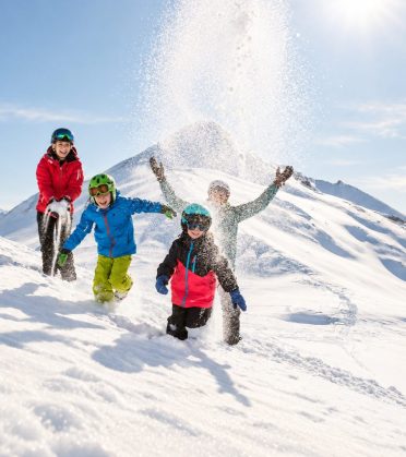 Drei Kinder toben im Schnee auf einem verschneiten Hang bei Serfaus.