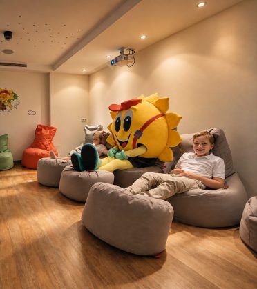 Mascot Sonni sitting with a child on beanbags in the children's cinema of Hotel DreiSonnen in Serfaus