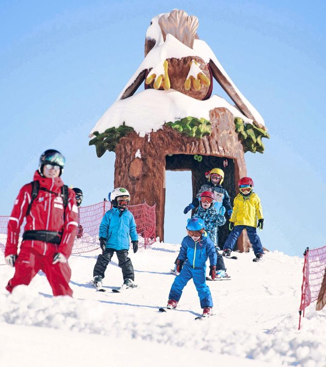Children in ski school riding through the wooden mascot gate on the practice slope.