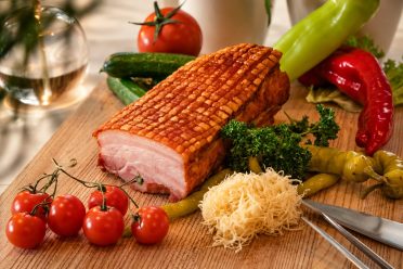 Roast pork with crackling on a wooden board with tomatoes, peppers and gherkins at Hotel DreiSonnen in Serfaus.