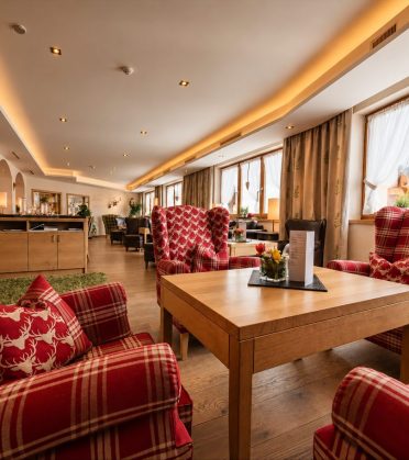 Loungebereich mit rot karierten Ohrensesseln und Holztischen im Hotel DreiSonnen.