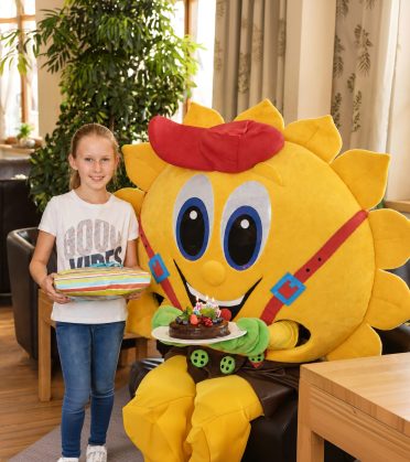 Mädchen mit dem Maskottchen Sonni und einer Geburtstagstorte.