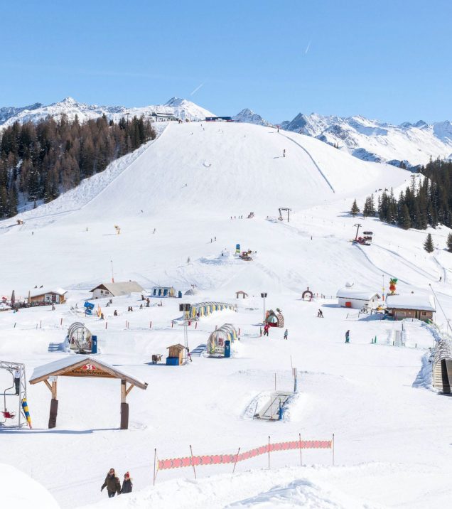 Das Kinderareal am Murmlipark mit Förderband, Hütte und flachen Übungshängen, dahinter die verschneiten Berge.