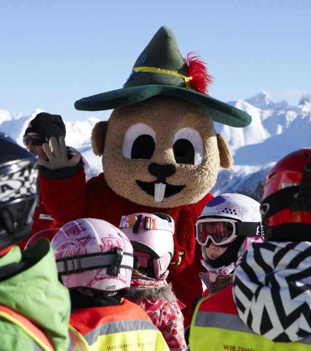 Das Murmli-Maskottchen steht zwischen Kindern mit Helmen und winkt in die Kamera.