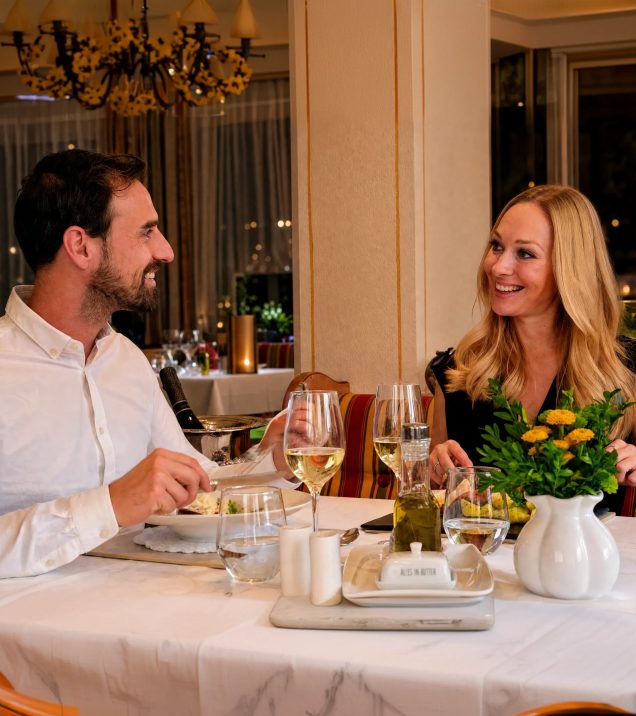 Paar beim Abendessen mit Weißwein im Speisesaal des Hotel DreiSonnen in Serfaus