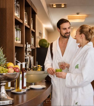 Paar im Bademantel steht mit Gläsern am Vitaminbuffet.