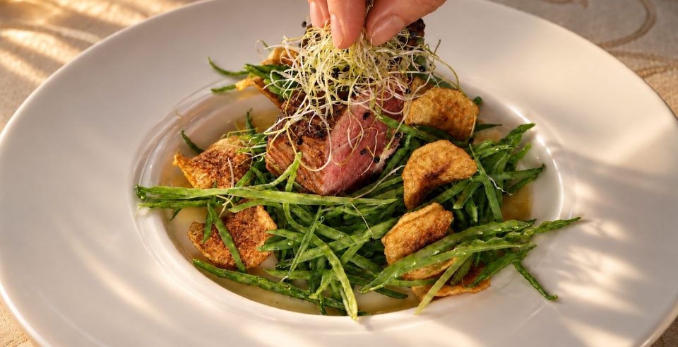 Rindersalat mit Rucola und Chips wird auf dem Teller angerichtet.