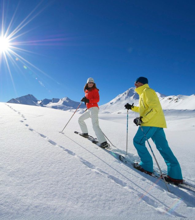 Zwei Personen stapfen im Gegenlicht nebeneinander durch den tiefen Schnee.