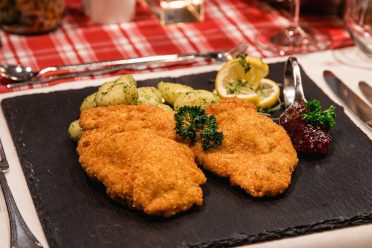 Two breaded schnitzels with parsley potatoes, lemon and lingonberries on a slate platter at Hotel DreiSonnen in Serfaus.