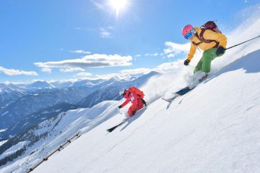 A skier in deep snow off the piste, backlit by the sun.