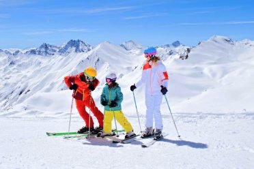 Ski instructor in a red jacket with two children on the piste against the mountain panorama.