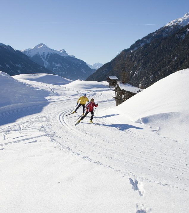 Ein Langläufer im Skating-Schritt auf der frisch gespurten Loipe, dahinter das weite verschneite Hochplateau.
