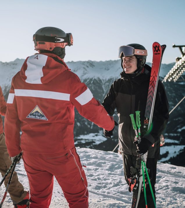 A ski instructor greeting a skier at the meeting point, skis on his shoulder.