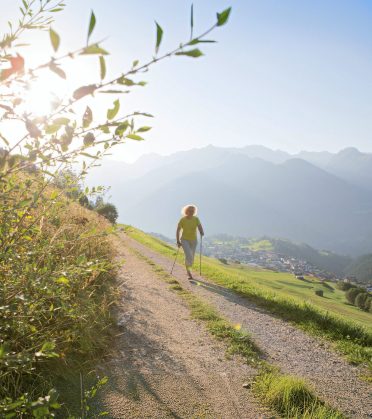 A person walks along a gravel path with Nordic walking poles, the mountains above the valley backlit.