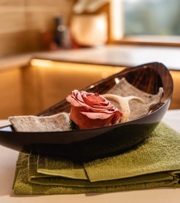 A rose in a wooden bowl on green cloths in the spa of Hotel DreiSonnen in Serfaus.