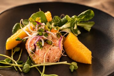 Tatar vom Räucherfisch mit Mango und Kresse auf einem dunklen Teller.
