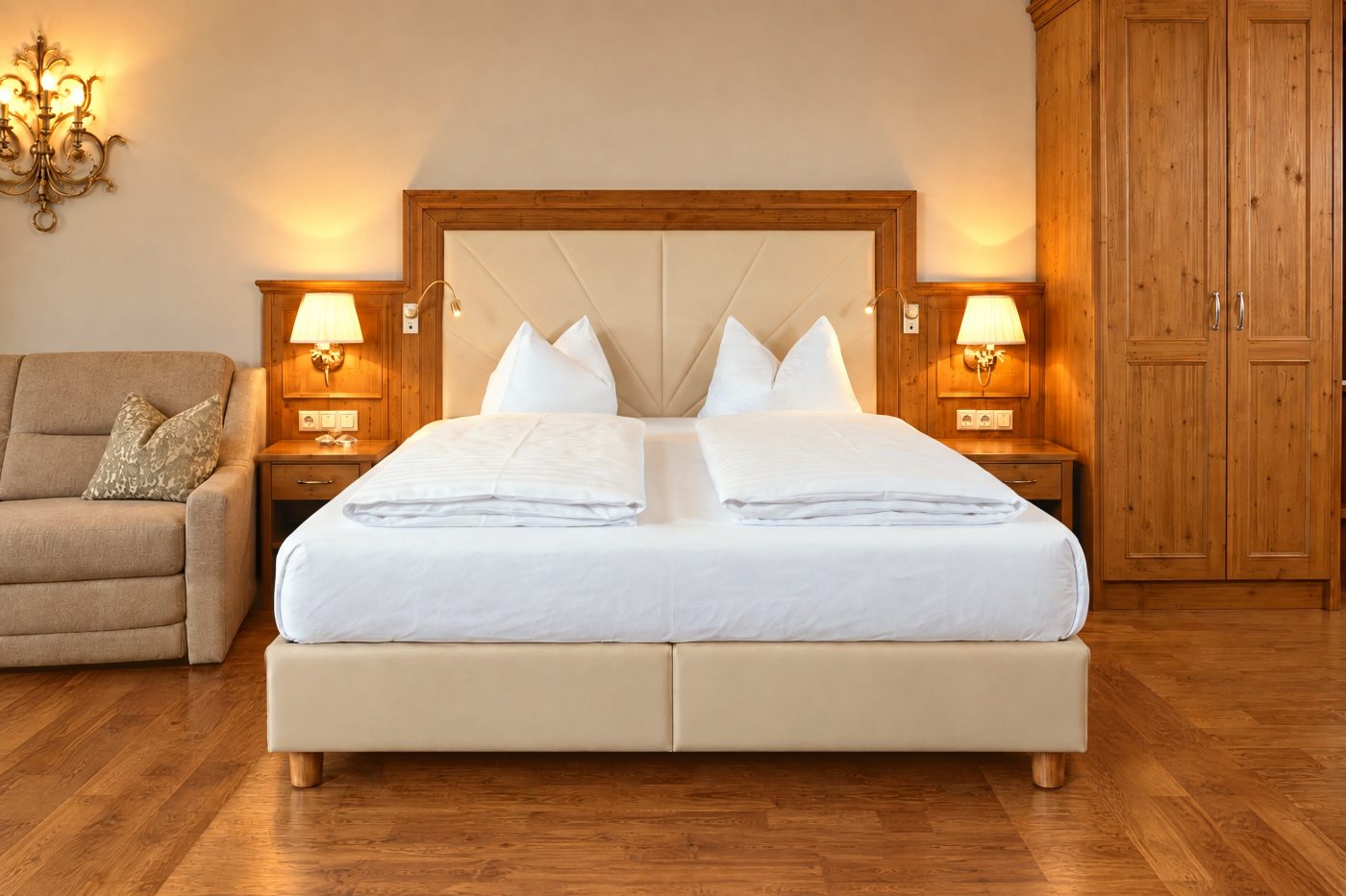 Doppelbett mit gepolstertem Kopfteil, Nachttischen mit Leselampen und Kleiderschrank im Zimmer Angela des Hotels DreiSonnen in Serfaus