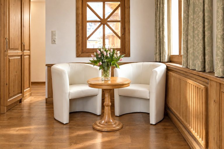 Seating area with two pale armchairs, a round wooden table and a bunch of tulips by the window in the Angela room at Hotel DreiSonnen in Serfaus