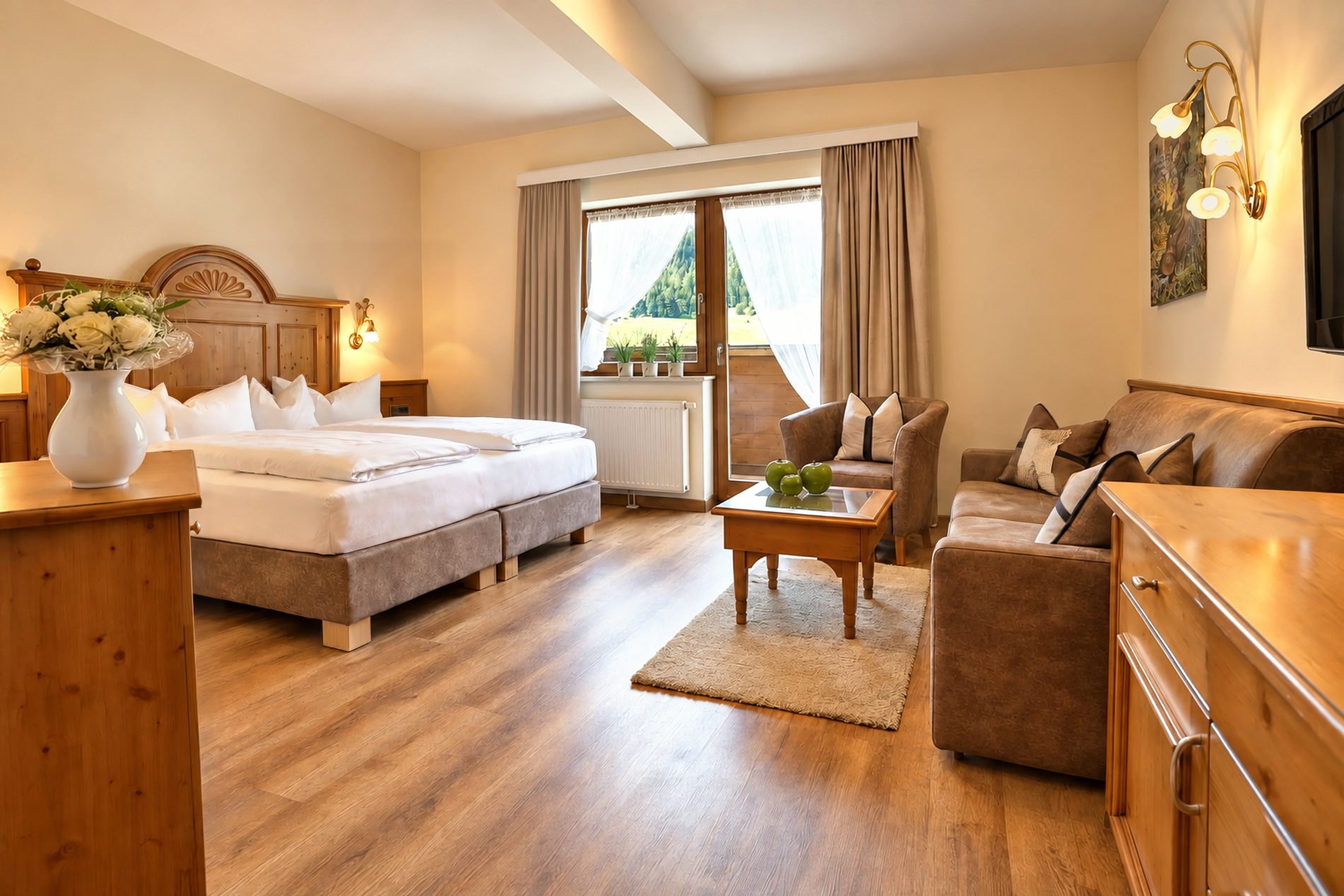 Doppelbett, Sitzgruppe und Balkontür mit Blick ins Grüne im Zimmer Anna Maria des Hotels DreiSonnen in Serfaus