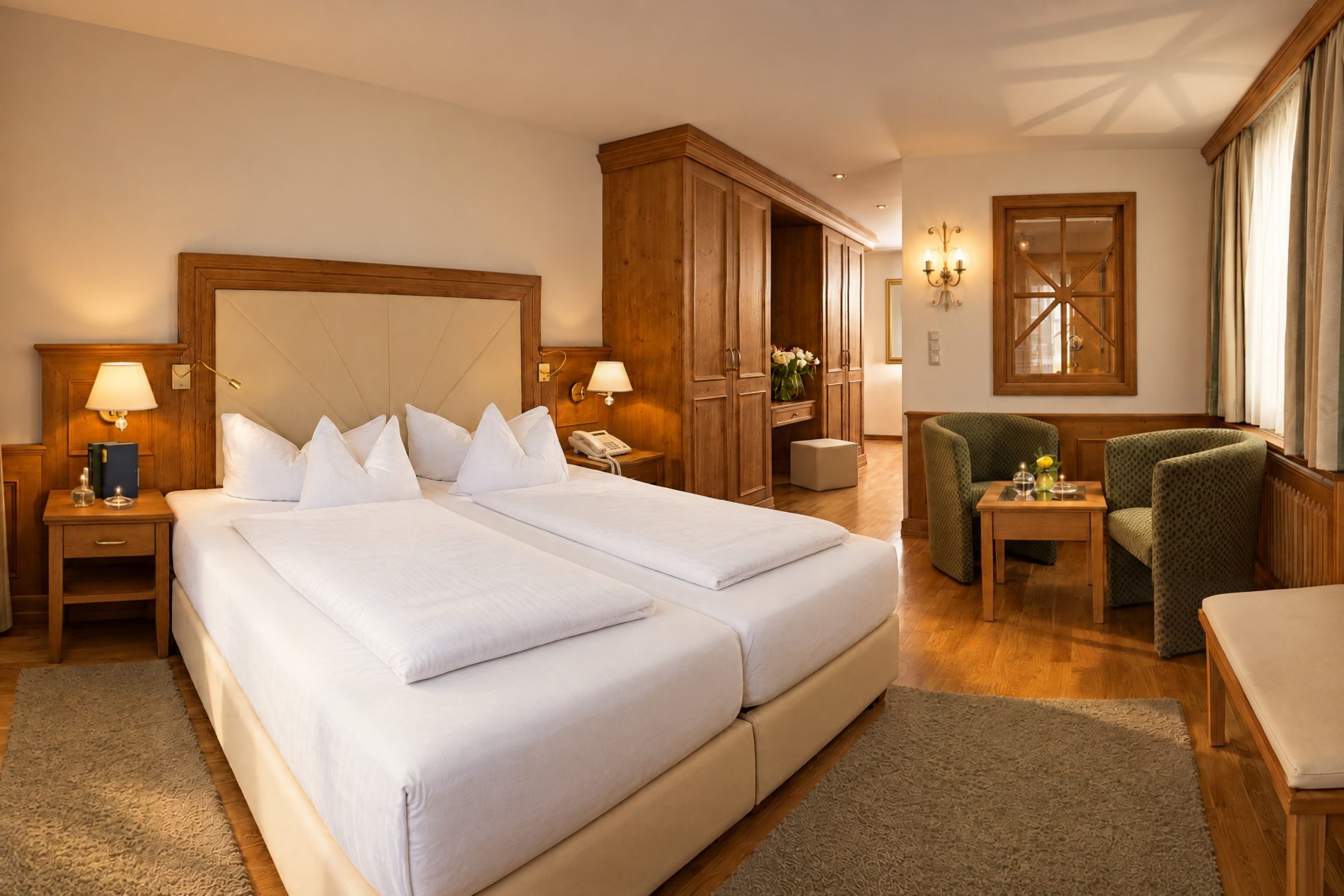 Deluxe-Suite Elias im Hotel DreiSonnen in Serfaus mit Doppelbett, Kleiderschrank aus Holz und Sitzecke mit zwei grünen Sesseln am Fenster